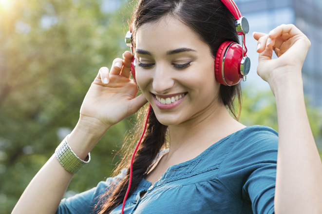 Closeup shot of young woman listening to music in a park. Portrait of happy smiling girl feeling free with music. Close up face of beautiful latin girl listening to music with professional headphone and dancing in a city center.